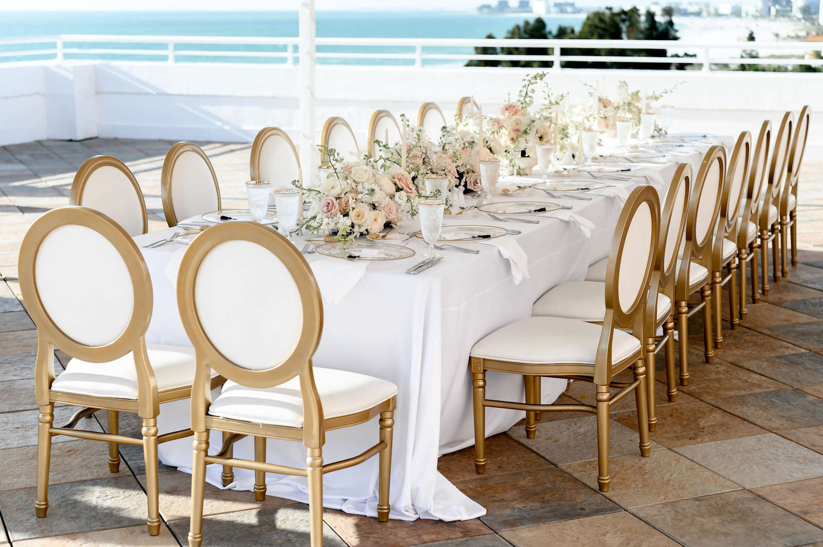 Elegant Classic Waterfront Rooftop Wedding Reception Decor, Long Feasting Table with Gold and White Dining Chairs, Low Floral Centerpieces and White Linens | Tampa Bay Wedding Planner Elegant Affairs by Design | Wedding Rentals Kate Ryan Event Rentals | Historic Pink Palace St. Pete Wedding Venue The Don CeSar Hotel