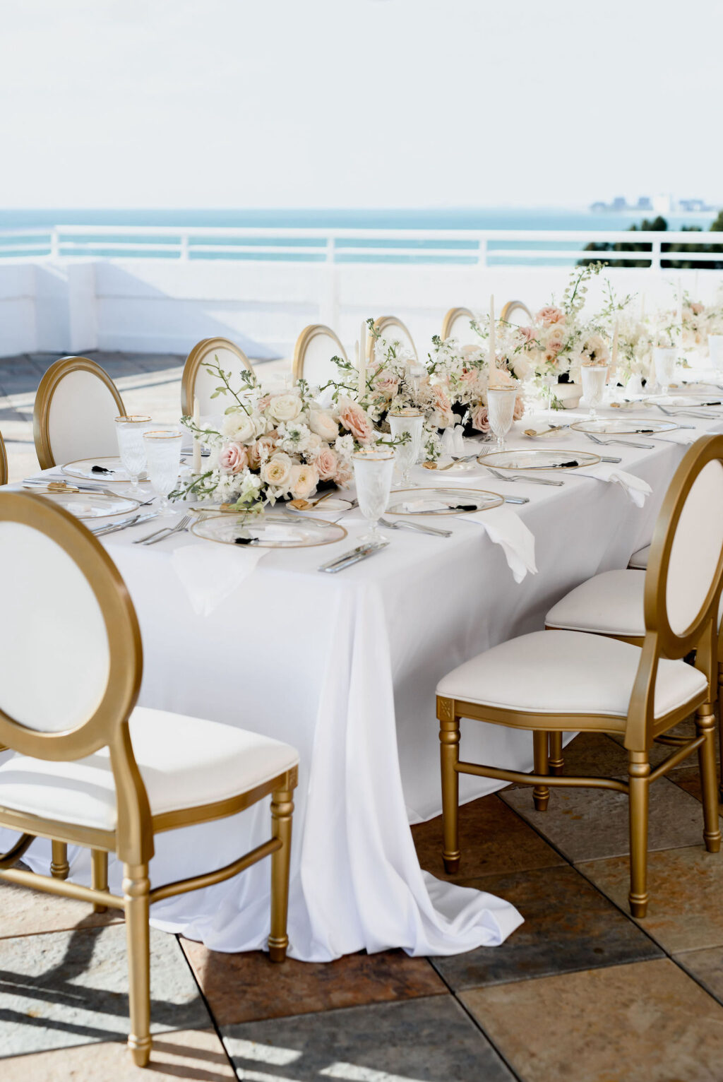 Elegant Classic Waterfront Rooftop Wedding Reception Decor, Long Feasting Table with Gold and White Dining Chairs, Low Floral Centerpieces and White Linens | Tampa Bay Wedding Planner Elegant Affairs by Design | Wedding Rentals Kate Ryan Event Rentals | Historic Pink Palace St. Pete Wedding Venue The Don CeSar Hotel