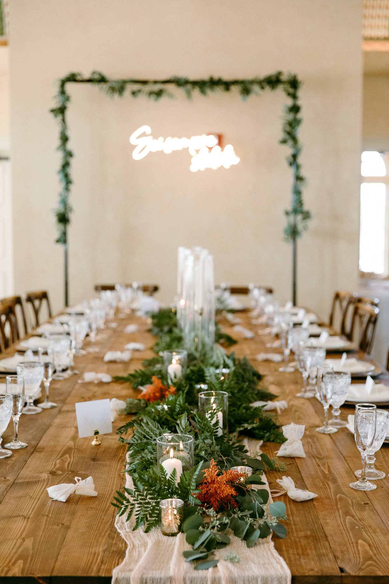 Rustic Italian Elegant Wedding Reception Decor, Ivory Cheesecloth Table Runner, Greenery, Candles, Neon Sign, Rectangular Arch with Greenery, Long Wooden Feasting Table | Tampa Bay Wedding Rentals Outside the Box Rentals