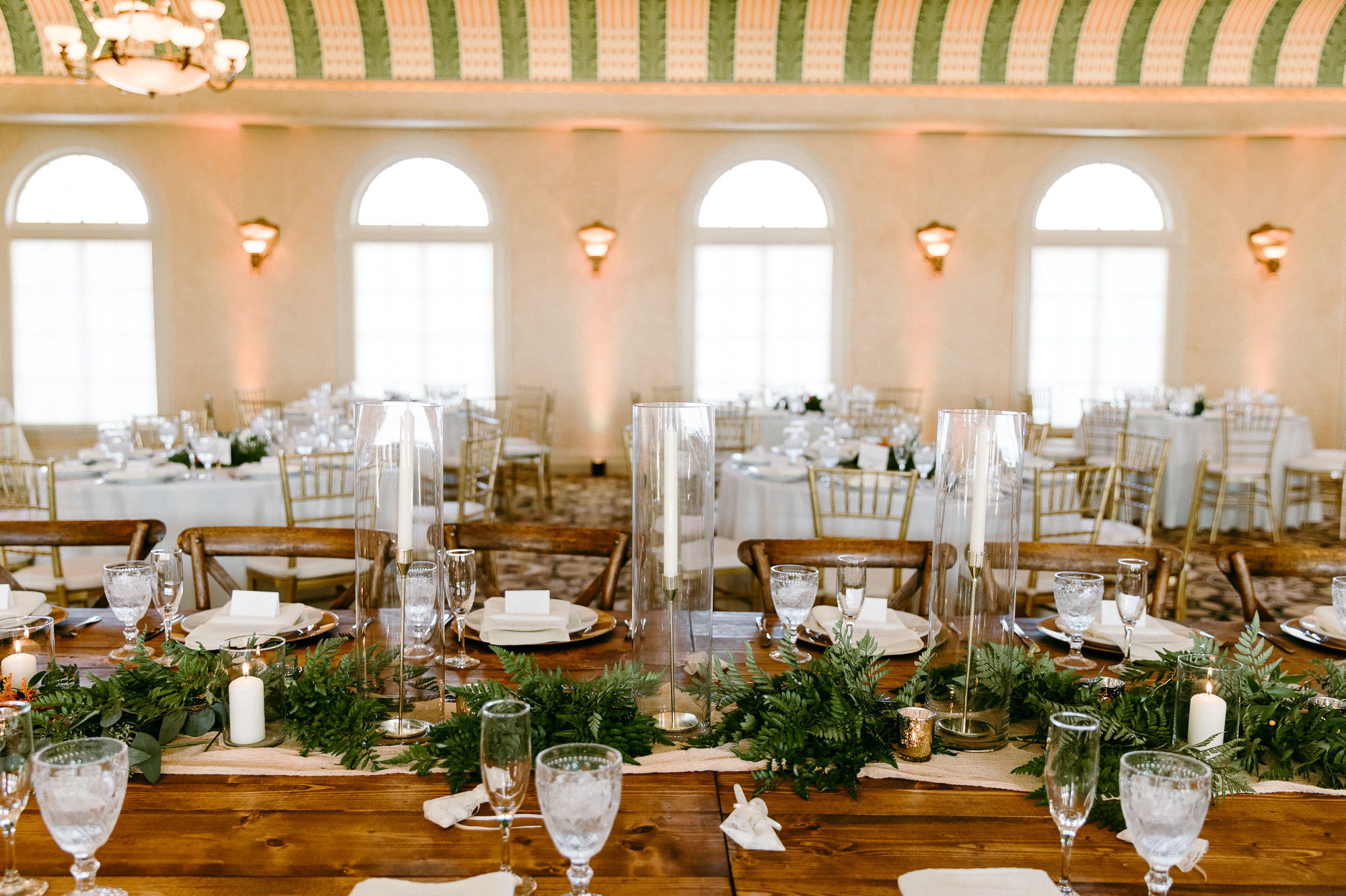 Rustic Italian Elegant Wedding Reception Decor, Ivory Cheesecloth Table Runner, Greenery, Candlesticks in Hurricane Glass Vases, Neon Sign, Rectangular Arch with Greenery, Long Wooden Feasting Table | Tampa Bay Wedding Rentals Outside the Box Rentals