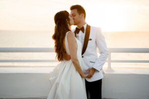 Romantic Classic Bride and Groom in White Tuxedo with Black Bowtie Sunset Rooftop Waterfront Wedding Portrait | Historic St. Pete Wedding Venue The Don CeSar Hotel