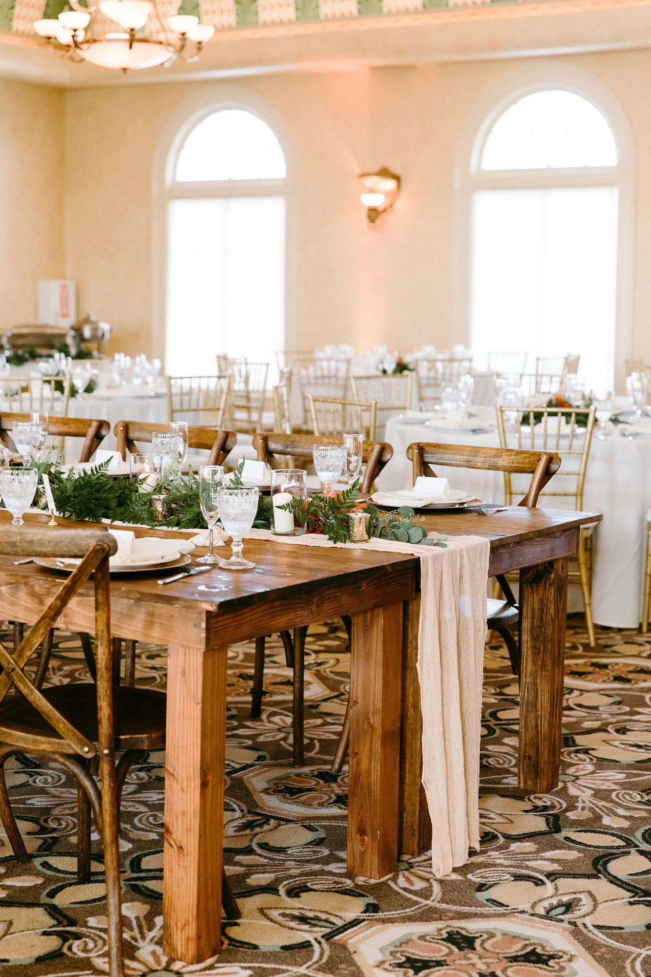Rustic Italian Elegant Wedding Reception Decor, Long Wooden Feasting Table with Wooden Cross Back Chairs, Ivory Cheesecloth Table Runner with Greenery, Candlesticks | Tampa Bay Wedding Rentals Outside the Box Rentals