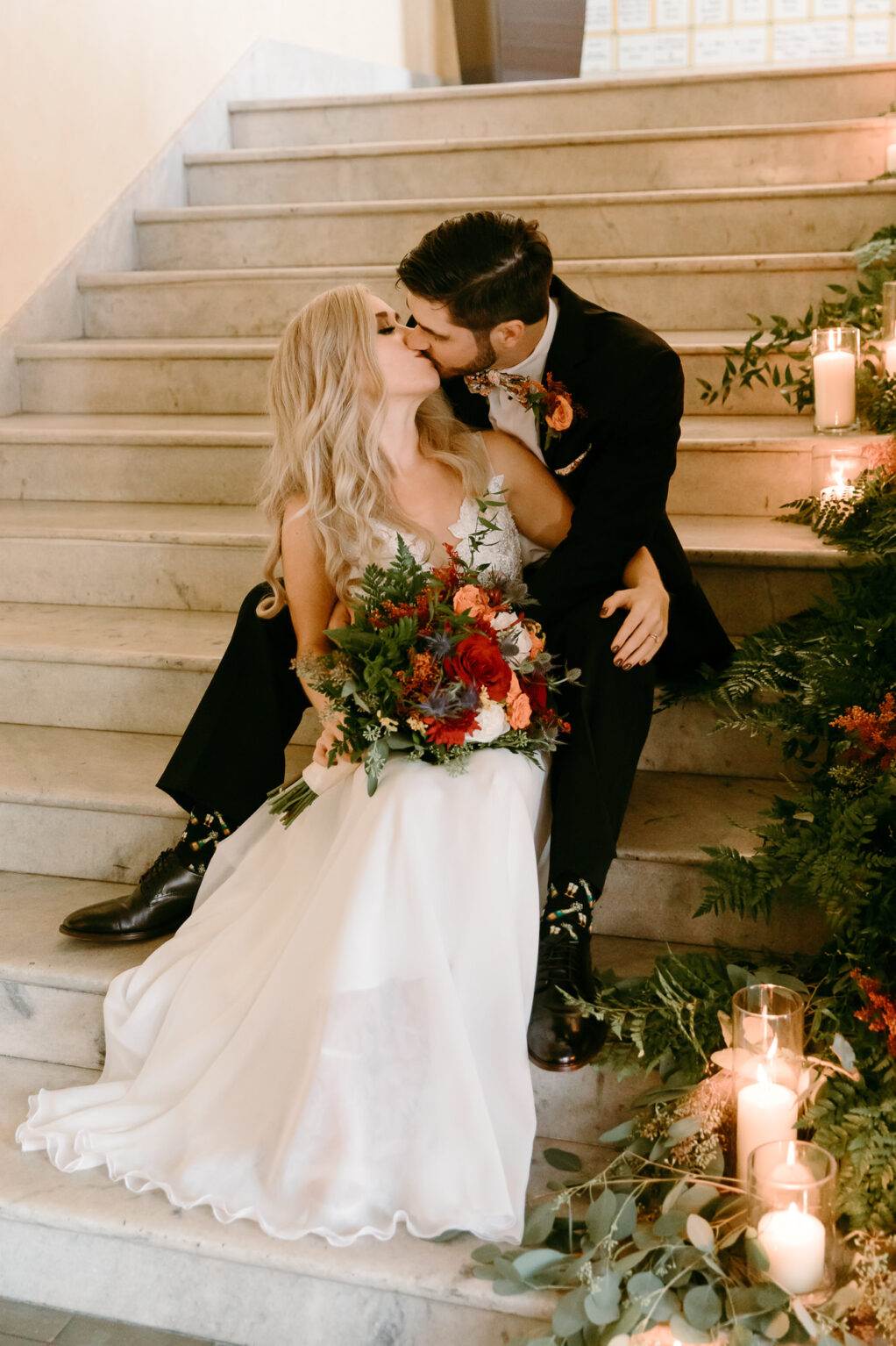 Bride and Groom Kissing on Staircase with Lust Flowers, Greenery and Candles