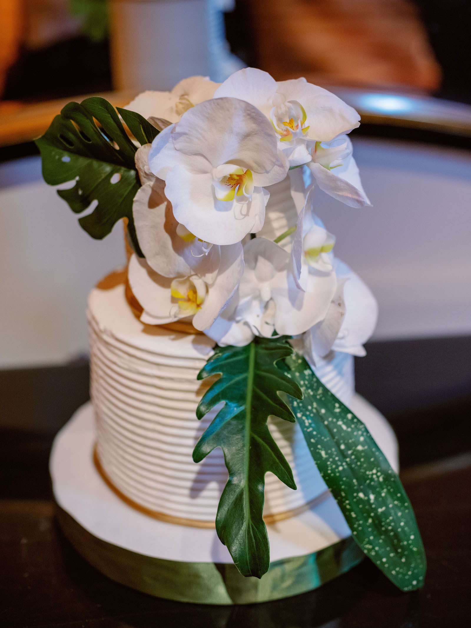 White and Green Modern Minimalist Tropical Wedding Reception, Simple Two Tiered White Textured Wedding Cake with Monstera Palm Leaves and White Orchid Flower Decor