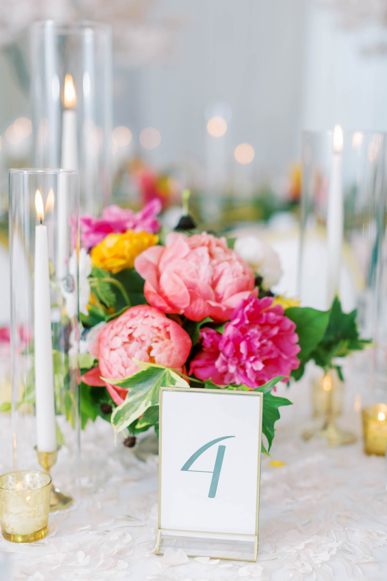 White and Gold Table Numbers with Tall White Candle Sticks and Gold Holders | Peony Centerpieces in Pink and Orange with Greenery