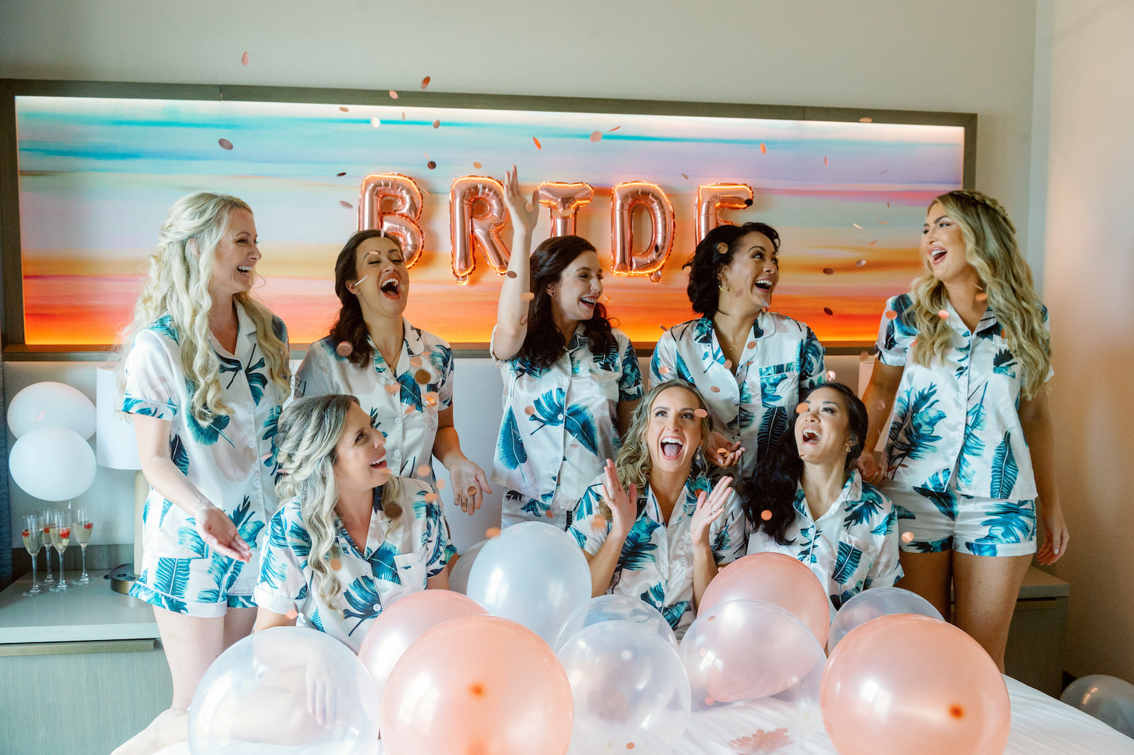 White and Green Modern Minimalist Tropical Wedding, Bride and Bridesmaids Getting Wedding Ready in Palm Tree Leaves Silk Short Pajama Set Throwing Confetti on Bed with Balloons | Tampa Hair and Makeup Femme Akoi Beauty Studio