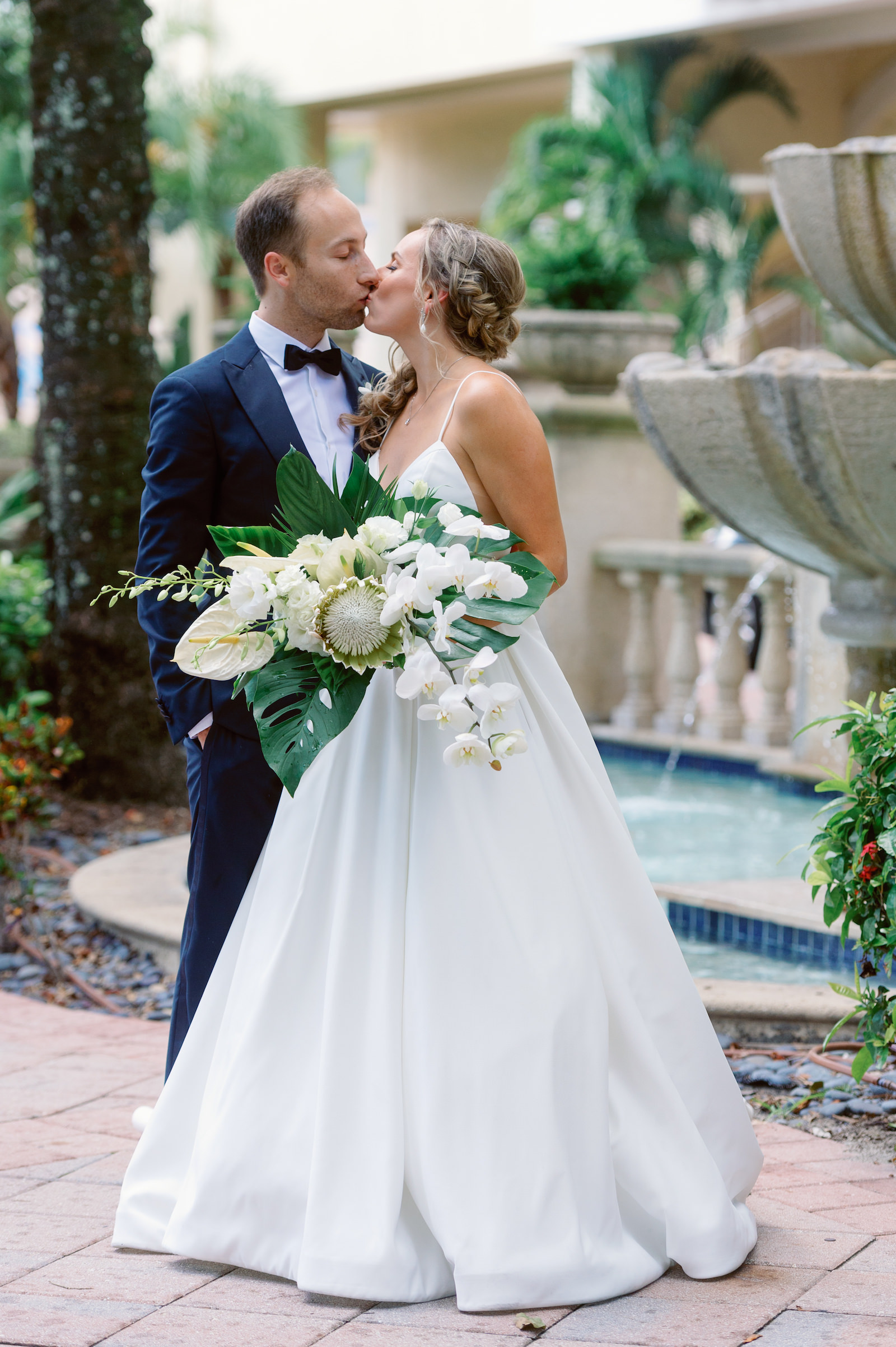 White and Green Modern Minimalist Tropical Wedding, Bride Wearing Chic Spaghetti Strap V Neckline A-Line Wedding Dress Holding White King Protea, Orchids, Roses and Anthurium with Palm Tree Leaves Floral Bouquet First Look with Groom | Tampa Bay Wedding Hair and Makeup Femme Akoi Beauty Studio