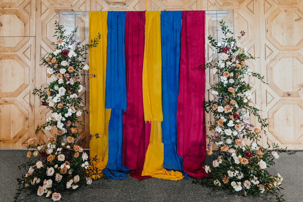 Modern and Edgy Fall Wedding Decor, Chic Gold Chairs, Greenery and Blush Pink, White and Mauve Roses Floral Arrangements Two Part Standing Floral Ceremony Arch, Primary Colors Yellow, Blue and Red Linen Draping | South Tampa Wedding Venue Hyde House | Wedding Rentals Kate Ryan Event Rentals
