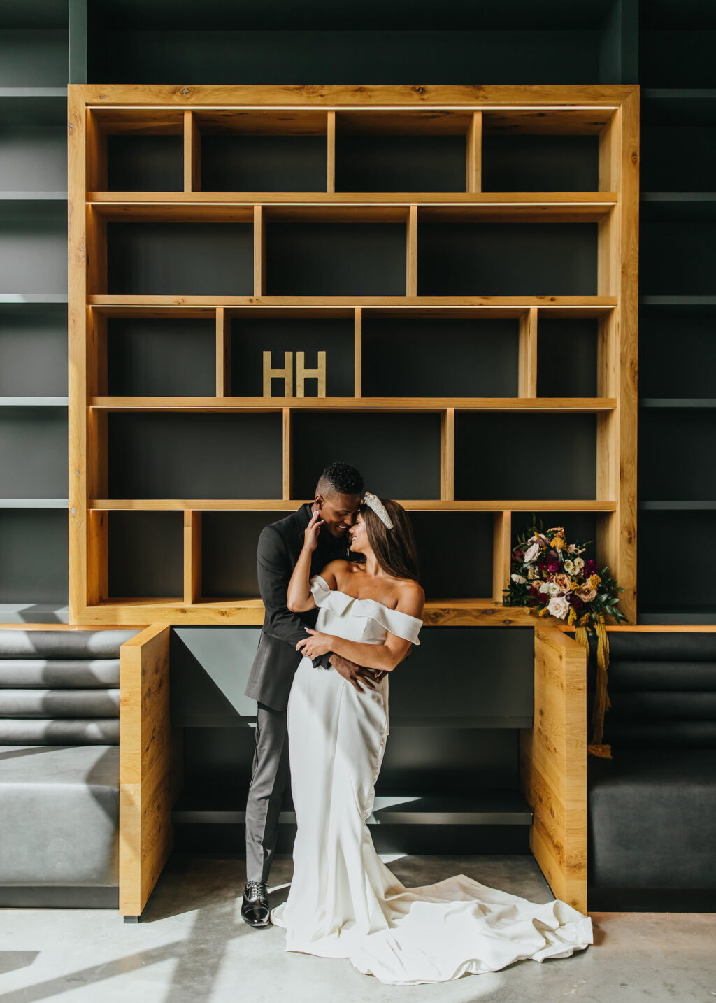 Modern and Edgy Fall Wedding, Tampa Bride Wearing Off the Shoulder Wedding Dress Holding Yellow, Burgundy Red and Blush Pink Roses Floral Bouquet with Greenery, Groom Wearing All Black Tuxedo and Peach Rose Boutonniere Sitting on Couch | Tampa Bay Wedding Venue Hyde House