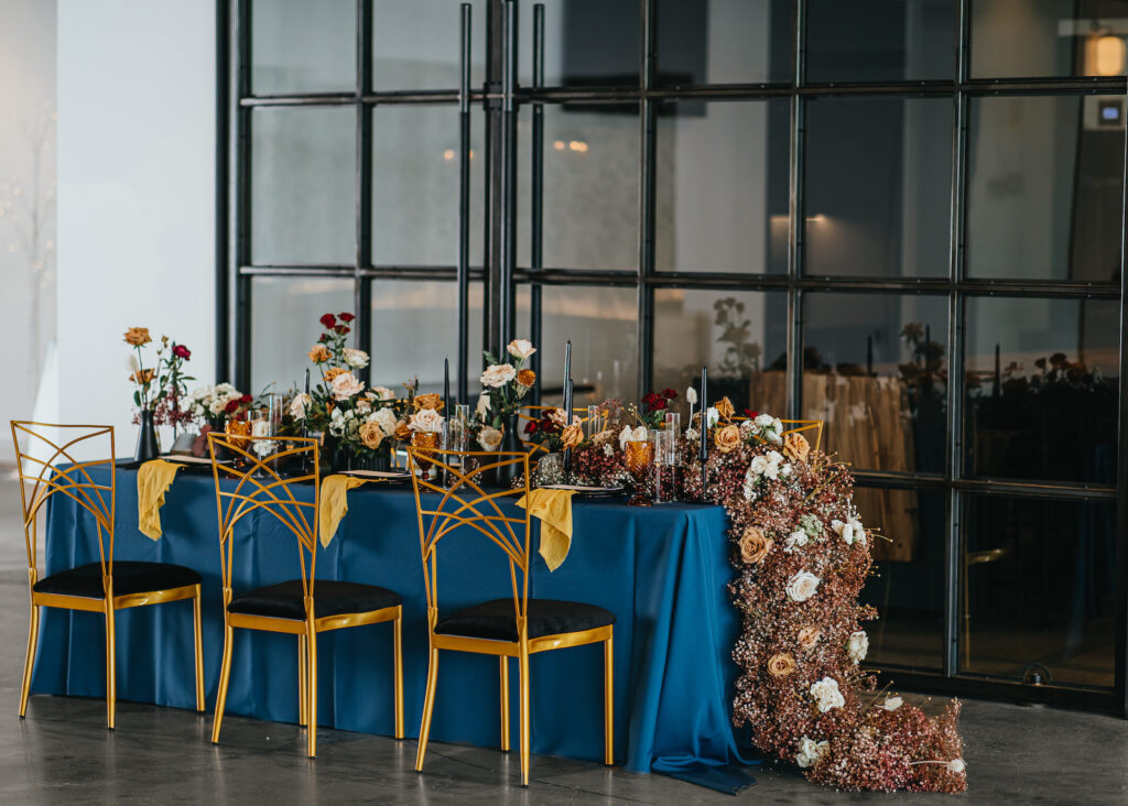 Modern and Edgy Fall Wedding Decor, Long Table with Royal Blue Table Linen, Lush Floral Table Runner, Chic Gold Chairs | South Tampa Wedding Venue Hyde House | Wedding Rentals Kate Ryan Event Rentals