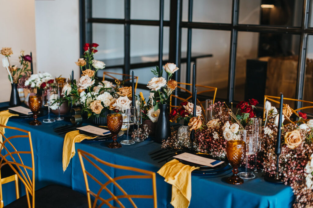 Modern and Edgy Fall Wedding Decor, Long Table with Royal Blue Table Linen, Yellow Linen Napkin, Lush Floral Table Runner, Chic Gold Chairs, Blue Candlesticks, Blush Pink and Dark Yellow Roses in Skinny Vases | Tampa Bay Wedding Venue Hyde House | Wedding Rentals Kate Ryan Event Rentals