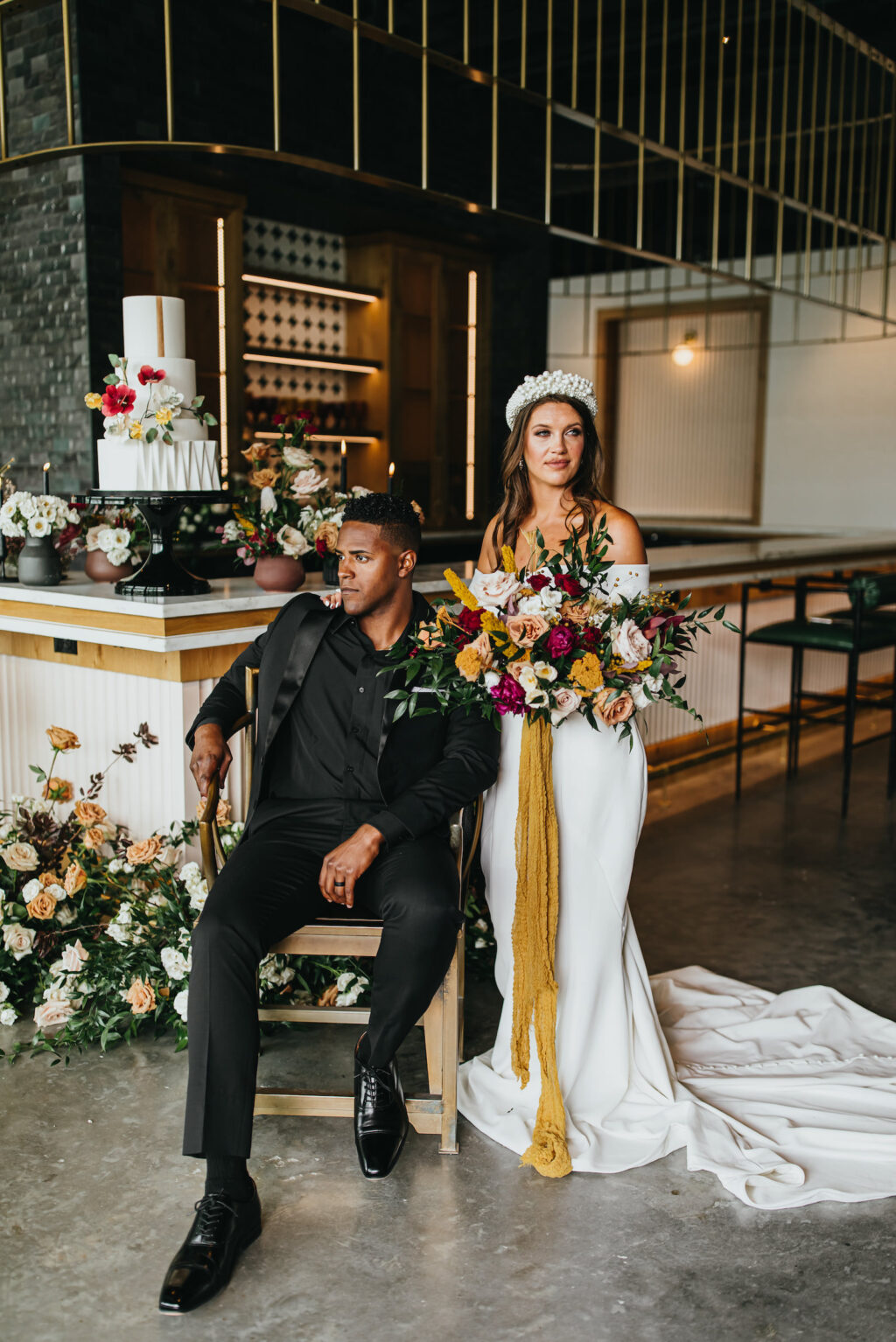Modern and Edgy Fall Wedding Reception, Groom Wearing All Black Tuxedo with Bride Wearing Off the Shoulder Wedding Dress, Thick Pearl Headdband, Holding Jewel Tone Floral Bouquet, Burgundy Red, White, Blush Pink and Yellow Roses with Greenery Flowers and Mustard Yellow Hanging Linen | Tampa Bay Wedding Venue Hyde House