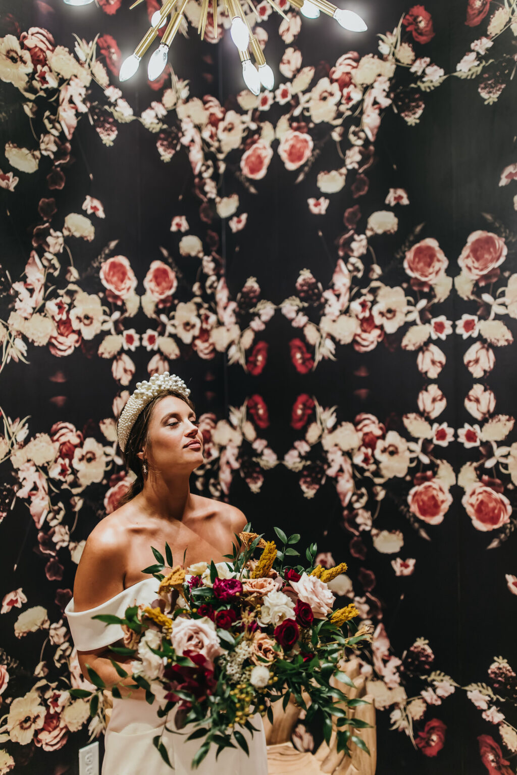 Modern and Edgy Fall Fall Wedding, Floral Black and Red Wall Backdrop, Bride Holding Blush Pink, Burgundy, Greenery and Yellow Floral Bouquet, Bride Wearing Off the Shoulder Wedding Dress and Elaborate Rhinestone Headband
