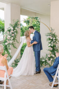 Bride and Groom First Kiss Portrait | Outdoor Elegant Wedding Ceremony with Gold and Floral Greenery Arch