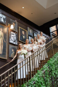 Modern Timeless Wedding Bridal Party on Staircase at Oxford Exchange, Bride Wearing Sequin Fitted Wedding Dress Holding White Floral Bouquet, Bridesmaids Wearing Matching Champagne Silk Dresses | Tampa Bay Wedding Photographer Lifelong Photography Studio