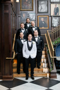 Modern and Timeless Black and White Wedding, Groom Wearing White and Black Tuxedo, Groomsmen in Black Tuxedos with Bowties Standing on Staircase at Wedding Venue Oxford Exchange | Tampa Bay Wedding Photographer Lifelong Photography Studio