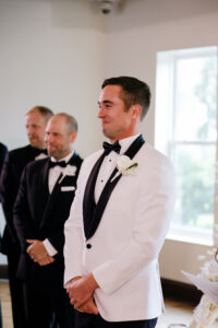 Modern and Timeless Wedding Ceremony Decor, Groom Wearing White and Black Tuxedo Reaction to Watching Bride Walking Down the Wedding Ceremony Aisle | Tampa Bay Wedding Photographer Lifelong Photography Studio