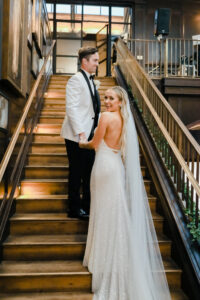 Modern Timeless Black and White Wedding, Bride Wearing Fitted Sequin Wedding Dress and Groom Wearing White and Black Tuxedo Climbing Staircase at Wedding Venue Oxford Exchange | Tampa Bay Wedding Photographer Lifelong Photography Studio