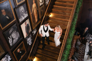 Modern Timeless Black and White Wedding, Bride Wearing Fitted Sequin Wedding Dress and Groom Wearing White and Black Tuxedo Climbing Staircase at Wedding Venue Oxford Exchange | Tampa Bay Wedding Photographer Lifelong Photography Studio