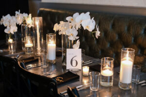Modern Timeless Black and White Wedding Reception Decor, Black Tables and Chairs, White Orchid Floral Arrangement Centerpieces, Candlesticks in Hurricane Glass Vases | Tampa Wedding Venue Oxford Exchange | Wedding Photographer Lifelong Photography Studio