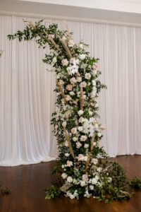 Romantic Indoor Garden Wedding Ceremony with Draped Backdrop, Curved Arch, and White and Greenery Florals