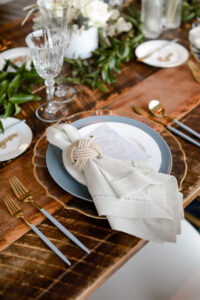 Romantic Blue Coastal Chic Wedding Reception Decor, White Linen Napkin, Wooden Table, Gold and Blue Flatware, Blue Plate, Gold Rimmed and Clear Glass Scalloped Charger, Rope Knot Napkin Ring Holder | Tampa Bay Wedding Photographer Lifelong Photography Studio | Wedding Rentals Kate Ryan Event Rentals