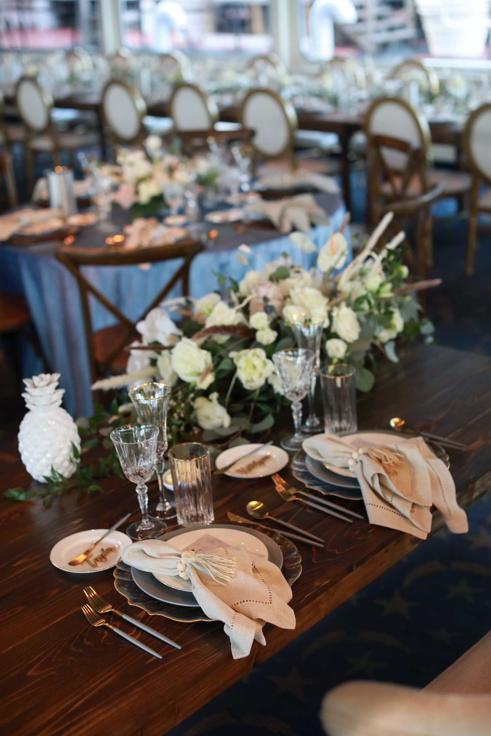 Romantic Blue Coastal Chic Wedding Reception Decor, Blue and Gold Silverware, White Linen Napkin, Wooden Table, Rope Nautical Knot Napkin Ring Holder, White Roses and Greenery Floral Arrangement | Tampa Bay Wedding Photographer Lifelong Photography Studio | Wedding Rentals Kate Ryan Event Rentals