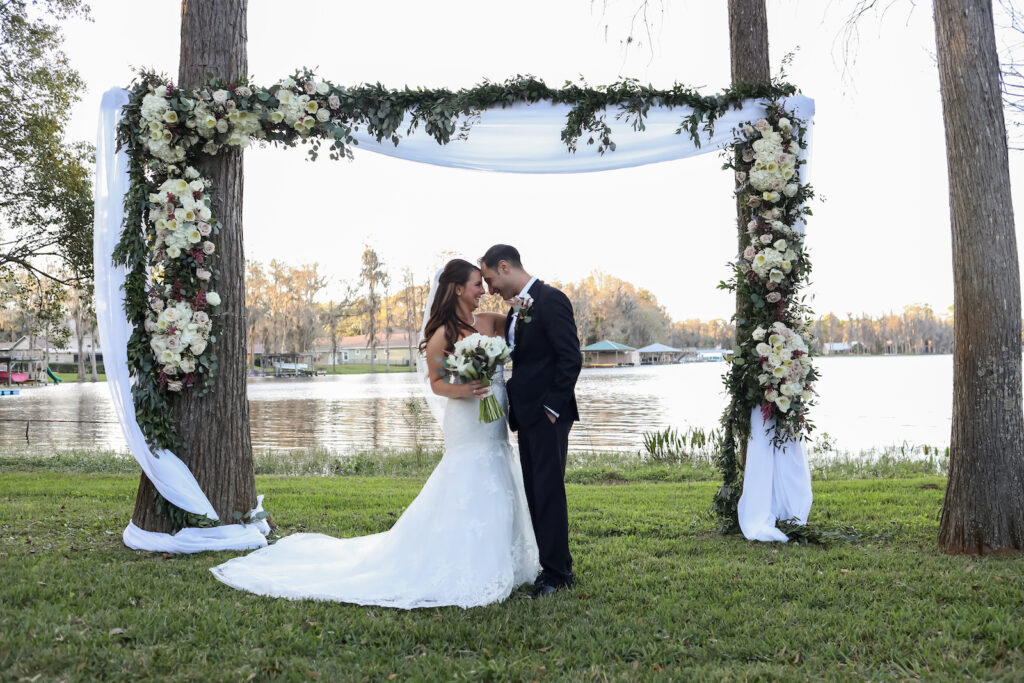 Romantic Classic Bride and Groom Exchanging Wedding Vows Outdoor Under Trees, Rectangular Arch Attached to Trees with White Linen Draping, White Floral Arrangements | Tampa Bay Wedding Photographer Lifelong Photography Studio | Wedding Planner Special Moments Event Planning | Wedding Dress Truly Forever Bridal