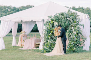 Bride and Groom Standing Under Rounded Greenery and White Tulip Floral Arch, Garden Whimsical Ceremony Wedding Decor, White Linen Tent, Greenery Arch with White Flowers At Outdoor Tampa Bay Wedding Venue Mill Pond Estate