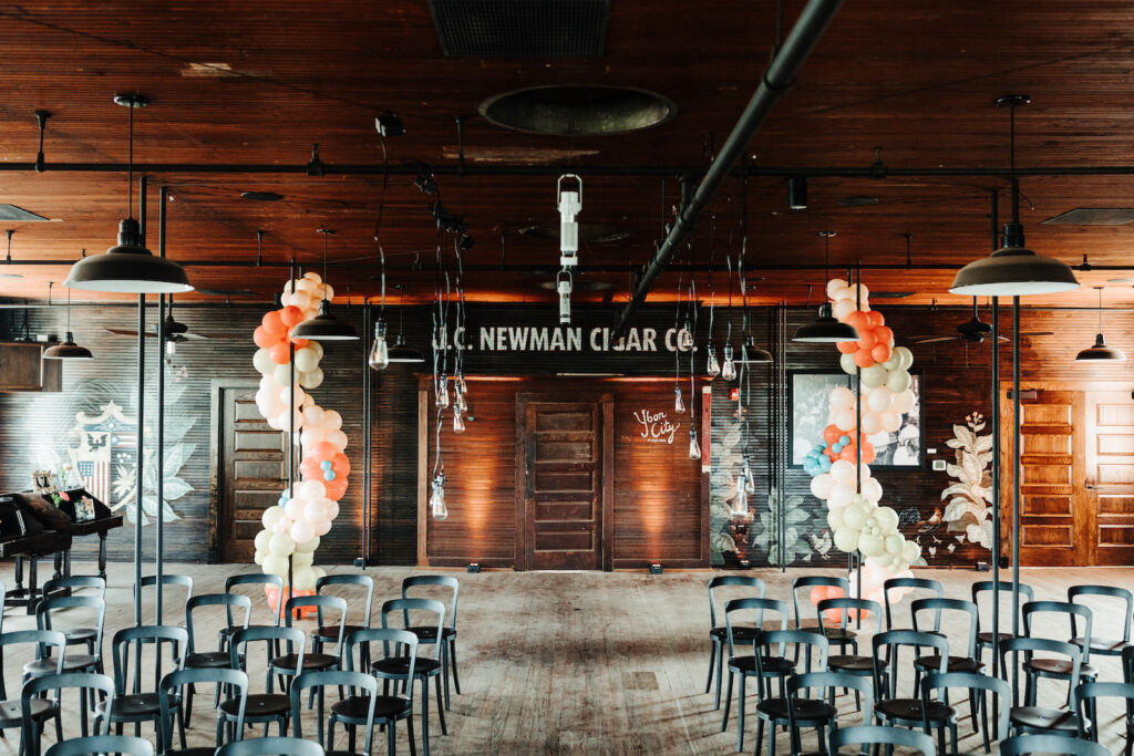 Industrial Indoor Wedding Ceremony with Balloon Arch Décor and Modern Black Chairs | JC Newman Cigar Factory Ybor Historic Wedding Venue