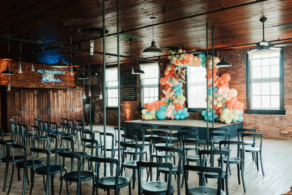 Industrial Indoor Wedding Ceremony with Balloon Arch Décor and Modern Black Chairs | JC Newman Cigar Factory Ybor Historic Wedding Venue