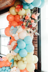Whimsical Orange, Yellow, and Blue Balloon Arch and Floral Décor for an Industrial Wedding Ceremony