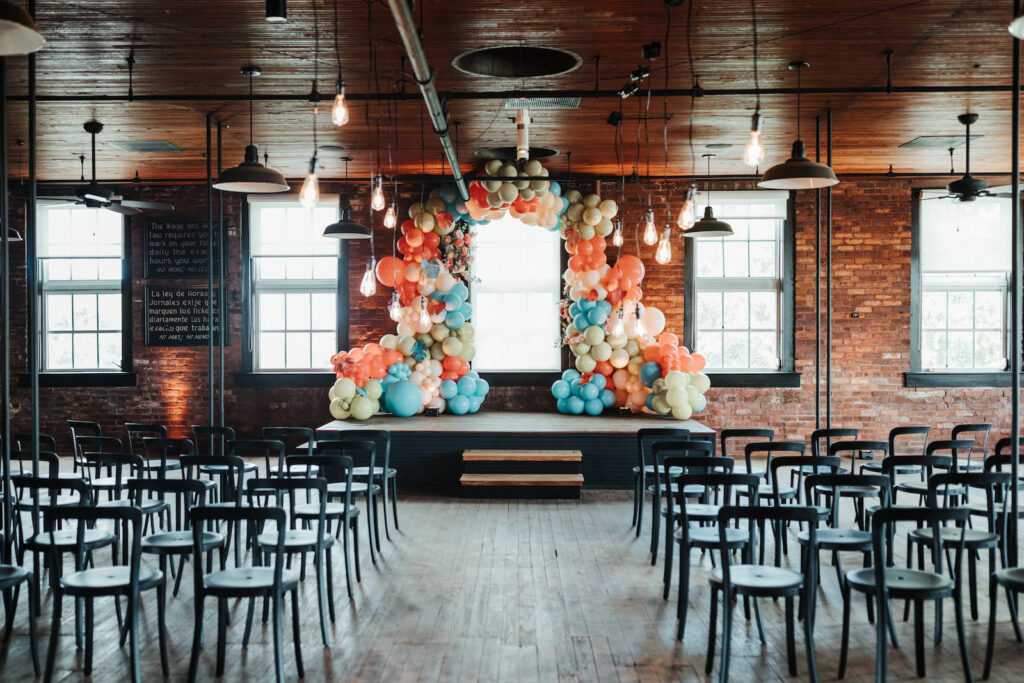 Industrial Indoor Wedding Ceremony with Balloon Arch Décor and Modern Black Chairs | JC Newman Cigar Factory Ybor Historic Wedding Venue