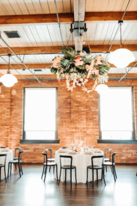 Industrial Indoor Wedding Reception with Hanging Floral Ceiling Installation, White Linens, Black Metal Chairs, and Red Brick Walls | JC Newman Cigar Factory Tampa Florida Wedding Venue