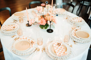 White and Gold Chargers with Patterned Orange Napkins Coral and Peach Flowers with Greenery Wedding Centerpieces with Tall Candles with Black Candle Stick Wedding Reception Décor Ideas