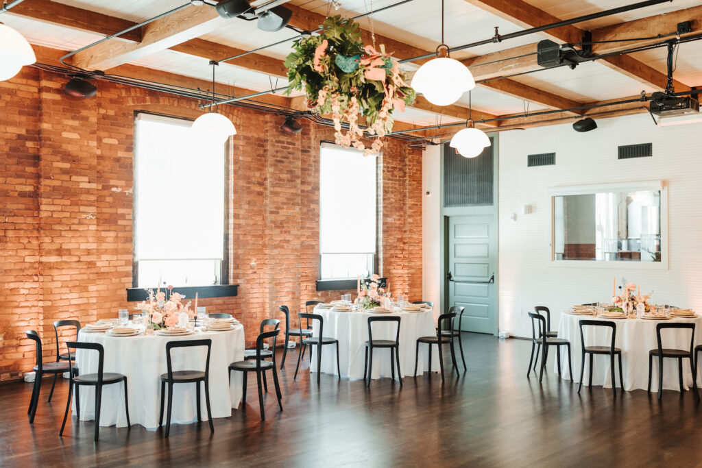 Industrial Indoor Wedding Reception with Hanging Floral Ceiling Installation, White Linens, Black Metal Chairs, and Red Brick Walls | JC Newman Cigar Factory Tampa Florida Wedding Venue