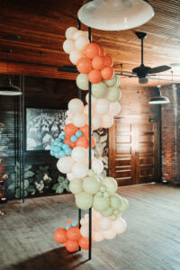 Whimsical Orange, Yellow, and Blue Balloon Arch and Floral Décor for an Industrial Wedding Reception