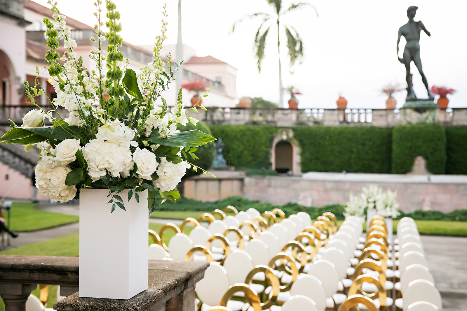 Luxurious Modern Chic Outdoor Courtyard Wedding Ceremony Decor, White Pedestal with Lush White Hydrangeas, Roses and Greenery Floral Arrangement, White and Gold Chairs | Tampa Bay Wedding Photographer Limelight Photography | Sarasota Wedding Venue Ringling Museum