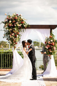 Elegant Garden Wedding Ceremony Decor, Bride and Groom Kissing Exchanging Vows, Wooden Arch with Lush Floral Arrangements and White Linen Draping | Tampa Bay Wedding Photographer Limelight Photography | Wedding Planner Breezin Weddings | Wedding Florist Lemon Drops | Wedding Rentals Outside the Box Event Rentals