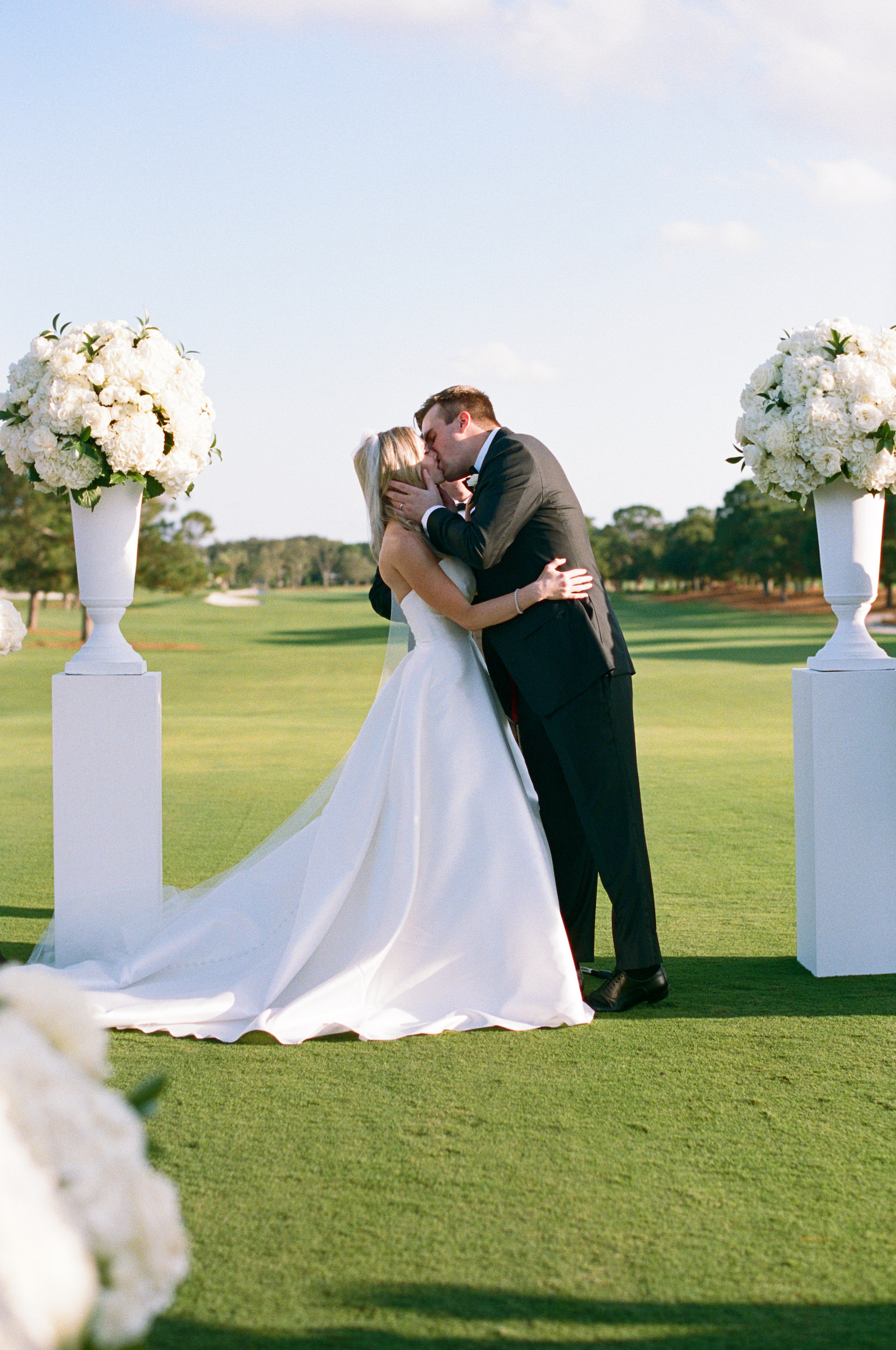 Bride and Groom Exchanging First Kiss, Luxurious Formal All White Outdoor Wedding Ceremony | Tampa Bay Wedding Florist Bruce Wayne Florals