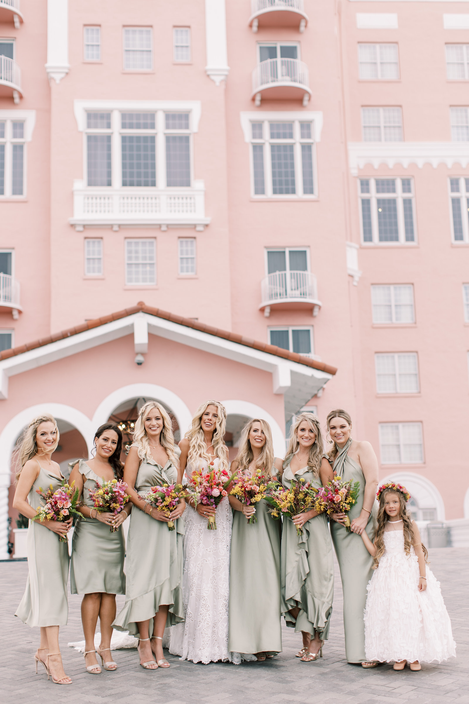 Vibrant Boho Wedding, Bride with Bridesmaids Wearing Mix and Match Sage Green Dresses Holding Hot Pink and Yellow Floral Bouquets, Flower Girl Wearing White Dress and Pink Flower Crown | Tampa Bay Wedding Hair and Makeup Femme Akoi Beauty Studio | St. Petersburg Waterfront Wedding Venue The Don CeSar