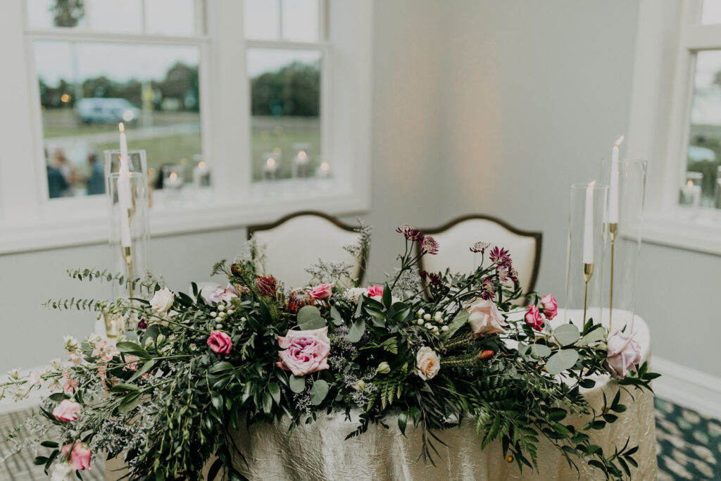 Wedding Reception Decor, Sweetheart Table with Lush Greenery, Blush Pink, Purple Roses, White and Gold Candlesticks | Tampa Bay Wedding Photographer Amber McWhorter Photography | Wedding Florist Leaf It To Us