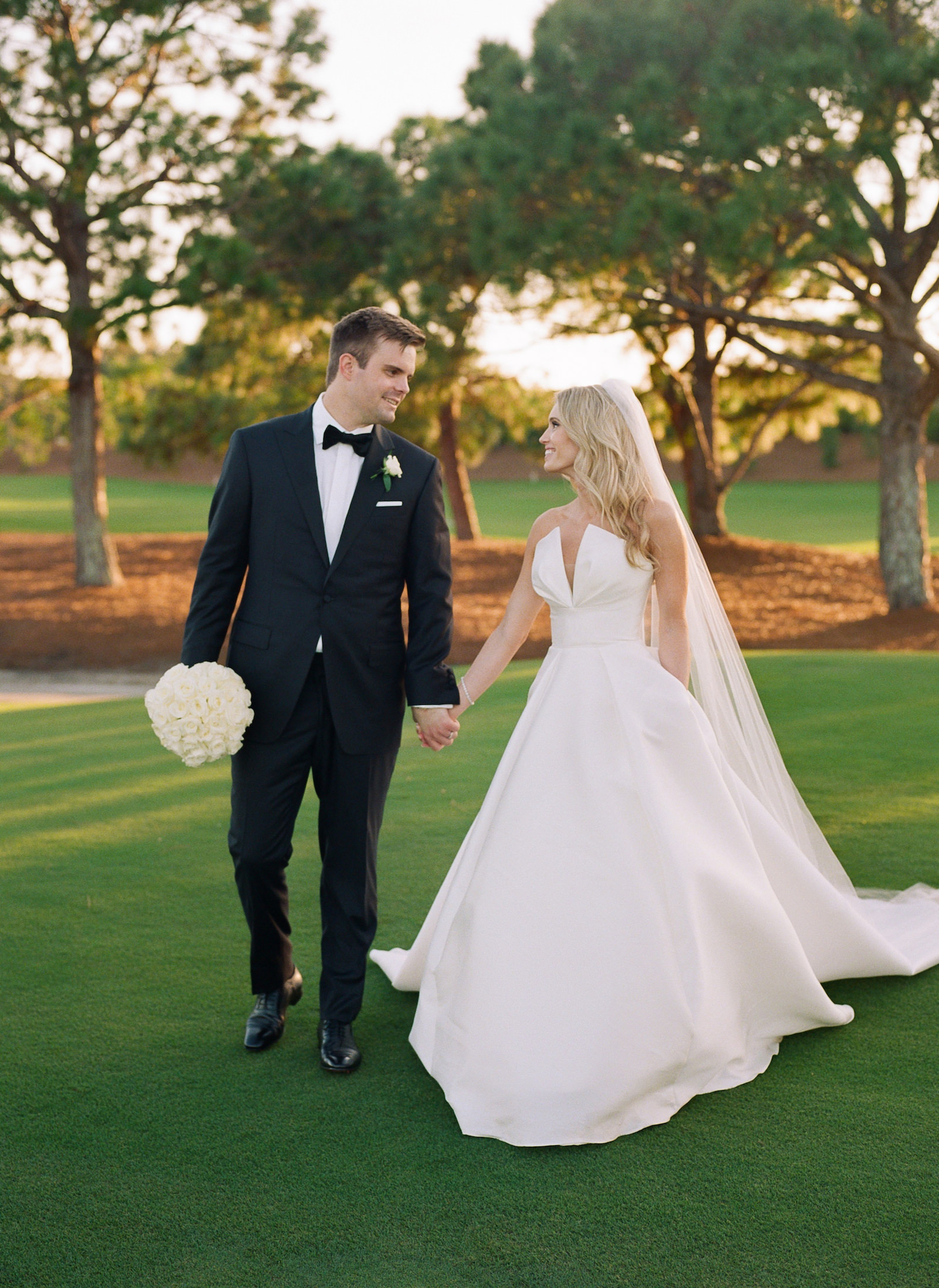 Luxurious Formal All White Wedding, Bride and Groom Holding Hands Walking on Golf Turf, Groom Holding All White Roses Floral Bouquet | Tampa Bay Wedding Florist Bruce Wayne Florals