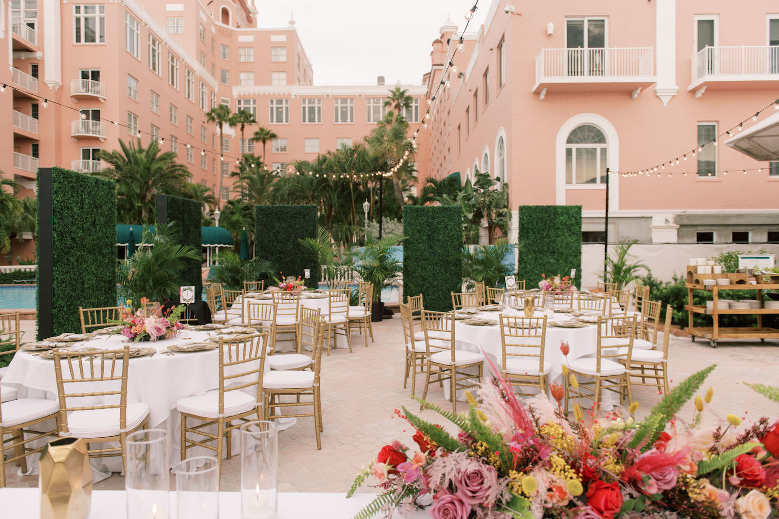 Vibrant Boho Courtyard Wedding Reception Decor, Gold Chiavari Chairs, White Linens, Low Floral Centerpieces, Hanging String Lights, Greenery Hedge Walls | St. Petersburg Waterfront Wedding Venue The Don CeSar