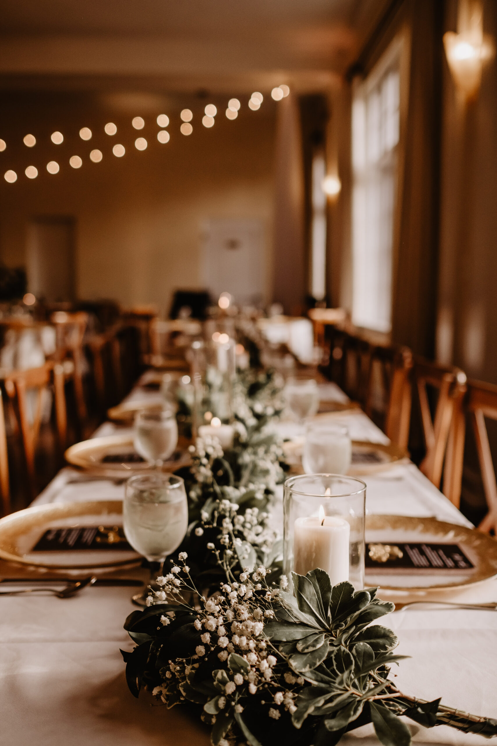Neutral Boho Modern Wedding Reception Decor, Long Feasting Table with White Linens, Wooden Cross Back Chairs, Greenery and Baby's Breathe Table Runner Garland | Tampa Bay Wedding Planner Taylored Affairs