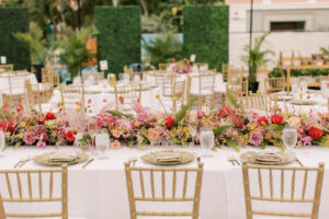 Vibrant Boho Wedding Reception Decor, Wedding Party Head Table, Gold Chiavari Chairs, Low Hot Pink and Red Roses, Pampas Grass, Craspedia Billy Balls, Greenery Low Floral Centerpieces, Hanging String Lights, Greenery Hedge Wall | St. Petersburg Historic Wedding Venue The Don CeSar