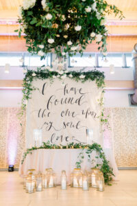 Wedding Quote Backdrop Behind Sweetheart Table in White and Greenery | Kate Ryan Event Rentals