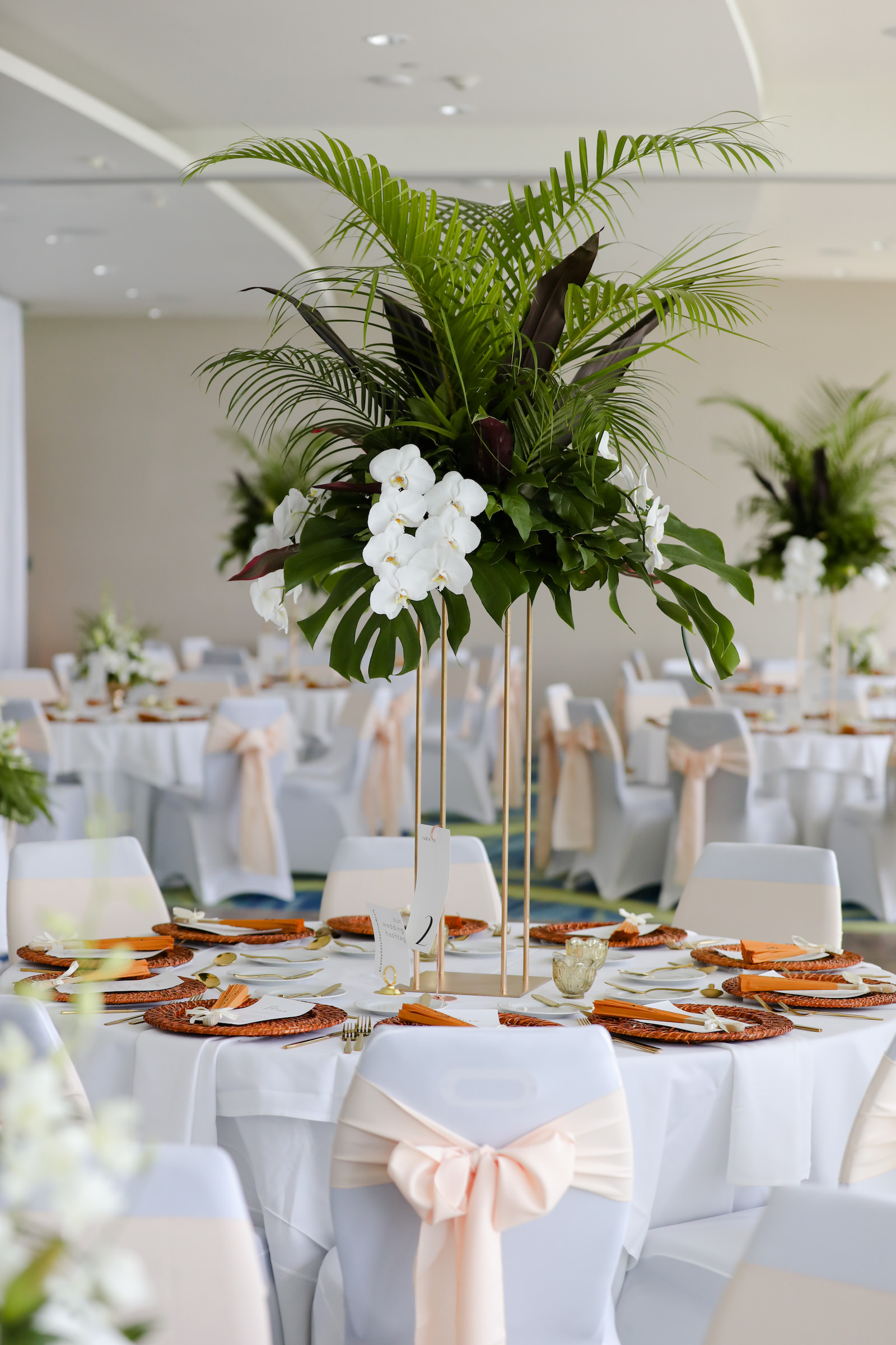 Modern Tablescape with Tall Gold Centerpieces with Greenery and White Flowers and Woven Chargers