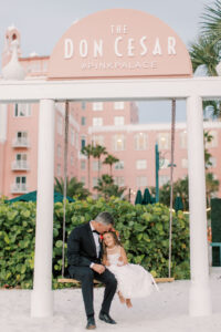 Groom Sitting on Beach Swing with Flower Girl | St. Petersburg Waterfront Historic Wedding Venue The Don CeSar