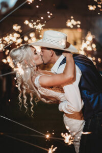 Beautiful Bride and Cowboy Groom Kiss During Sparkler Exit Wedding Portrait